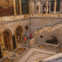People walking in a marble-floored museum with statues, archways, and large paintings on the walls.