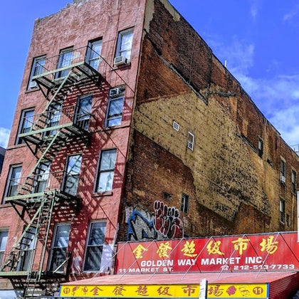 A brick building with a fire escape and a sign for Golden Way Market Inc in English and Chinese under a blue sky.