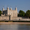 Historic stone fortress with turrets and battlements, located beside a river with trees in the background under a clear sky.