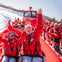 People wearing red jackets smiling and raising their hands while enjoying a ride on a red speedboat.