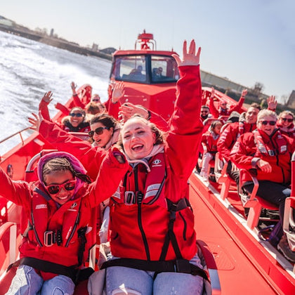 People wearing red jackets smiling and raising their hands while enjoying a ride on a red speedboat.