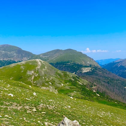 A scenic view of green rolling hills and distant mountains under a clear blue sky.