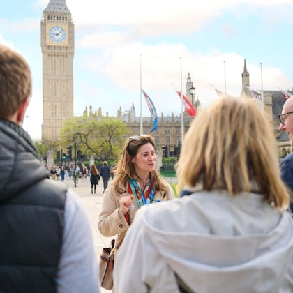 A tour guide speaking to a group of people near the Big Ben tower in London on a sunny day.