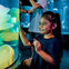 A young girl smiling and touching the glass of an illuminated aquarium exhibit, with blurred figures and tanks in the background.