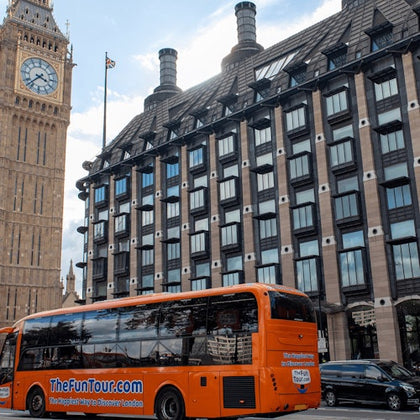 An orange tour bus parked in front of a building with many windows, with Big Ben visible in the background.
