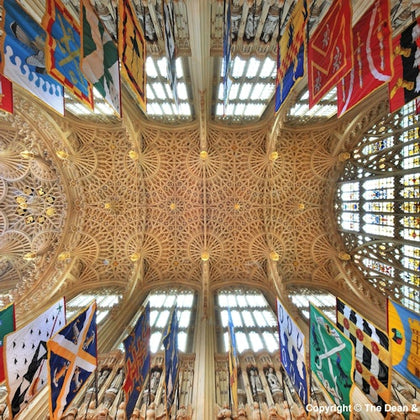 Ornate cathedral ceiling with intricate designs and large stained glass windows, adorned with colorful banners.