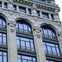 A portion of a building facade with arched windows, decorative stone details, and ornate metal railings.