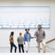 A group of people in a gallery with a large abstract painting of rounded shapes on the wall behind them.