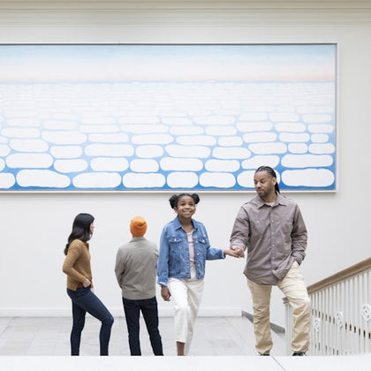 A group of people in a gallery with a large abstract painting of rounded shapes on the wall behind them.