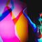 Person in a cap interacting with a multicolored light installation, casting overlapping shadows on the wall.