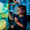 A young girl smiles and touches an illuminated aquarium, with glowing jellyfish inside. A child is visible in the background.