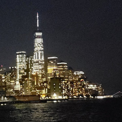 A city skyline at night with illuminated skyscrapers reflected on water, dominated by a tall, lit tower.