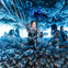 A person smiling in a room filled with black balloons, with others in the background under blue lighting.