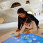 A woman and child interact with a touch-screen exhibit in a modern museum with curved, beige walls in the background.
