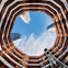 Upward view through an octagonal structure with copper-colored lining, revealing skyscrapers and blue sky with scattered clouds.