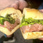 A sandwich with meat, greens, and cheese on crusty bread being held up by two hands.