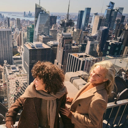 Two people smiling on a rooftop overlooking a city skyline with tall buildings under a clear sky.