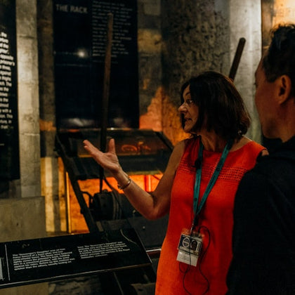 A woman in an orange dress giving a tour to a man, with historical exhibits and information panels in the background.