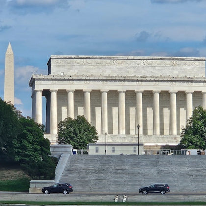 The Lincoln Memorial with the Washington Monument in the background, framed by greenery and a wide staircase in the foreground.