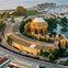 Aerial view of the Palace of Fine Arts in San Francisco, surrounded by greenery and water, with a marina and bay in the background.