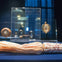 A collection of ornate jewelry displayed in glass cases, with a pearl and tassel necklace in the foreground on a blue surface.