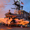 A military aircraft, marked "602," is parked on the deck of a ship with a large structure marked "41" and various flags in the background.