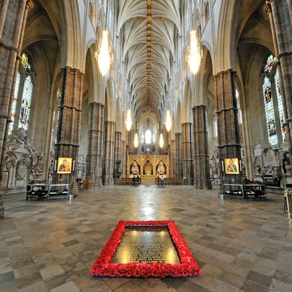 Interior view of a grand cathedral with high vaulted ceilings, chandeliers, and a memorial surrounded by red flowers on the floor.