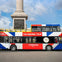 A double-decker bus with a Union Jack design and "The Original Tour" branding, parked near a column monument on a sunny day.