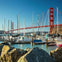 A marina with boats docked in the foreground and the Golden Gate Bridge spanning over the water in the background.