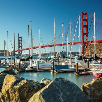 A marina with boats docked in the foreground and the Golden Gate Bridge spanning over the water in the background.