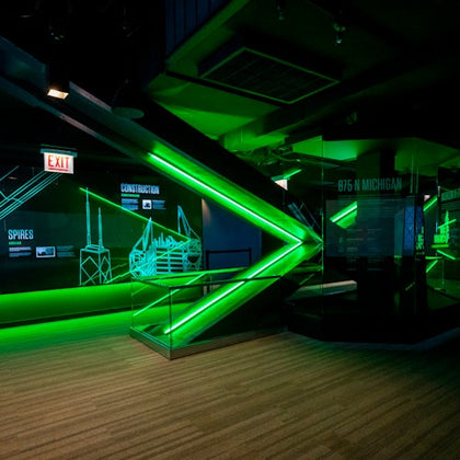 A modern exhibit with green neon lighting, displays about architecture, and a sleek, futuristic design.