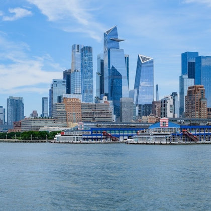 City skyline with modern skyscrapers and waterfront buildings, viewed from across a body of water under a blue sky.