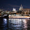 A boat labeled 'Uber Boat by Thames Clippers' docked on a river at night, with illuminated buildings and a dome in the background.