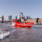 A red speedboat labeled "Thames Rockets" travels on the River Thames in London, with city landmarks in the background.