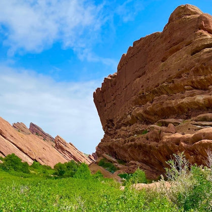 Red rock formations rise above a green field under a partly cloudy blue sky.