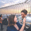 People enjoying the view from a fenced observation deck at sunset, with a cityscape visible in the background.