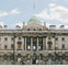 A neoclassical building with columns and a central dome, featuring a flag on top, with people in front on a sunny day.