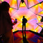 A person photographing another silhouetted against a colorful geometric background in a reflective room.