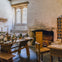 A rustic room with wooden furniture, a large fireplace, candles, glassware, and a multi-paned window.