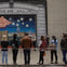 A group of people stand in front of a mural featuring a U.S. flag and stars on a building facade.