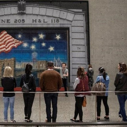 A group of people stand in front of a mural featuring a U.S. flag and stars on a building facade.