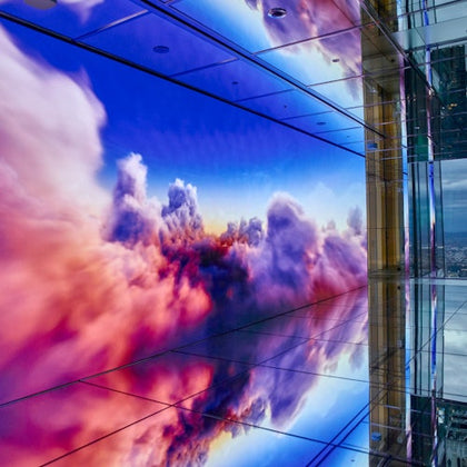 A digital display showing colorful clouds reflected on a glossy floor in a modern indoor setting.