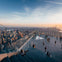 People on a rooftop observation deck with glass railings, overlooking a cityscape at sunset.