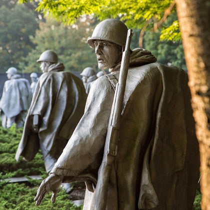 A group of soldier statues in a park setting, surrounded by greenery and trees, with one statue prominently in the foreground.