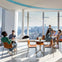 People sitting at modern tables by large windows with a cityscape view, in a bright and stylish interior space.