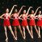 Five dancers in matching red sequined outfits perform on stage under star-like lights, posing with arms raised.