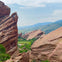 Rocky landscape with large red sandstone formations and a lush green valley in the background under a cloudy sky.
