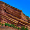 A large red rock formation with steps and trees in the foreground under a clear blue sky.