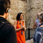 A tour guide in an orange dress talks to a group of people in front of a stone wall.