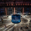A large blue cylindrical installation emits light trails in a dimly lit industrial space with people observing.